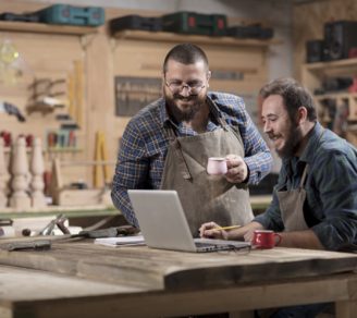 Two small business owners in their workshop, researching on a laptop