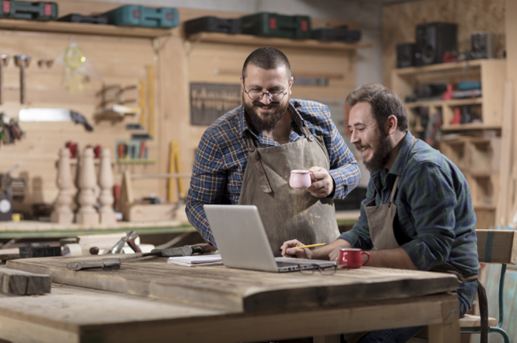 Two small business owners in their workshop, researching on a laptop