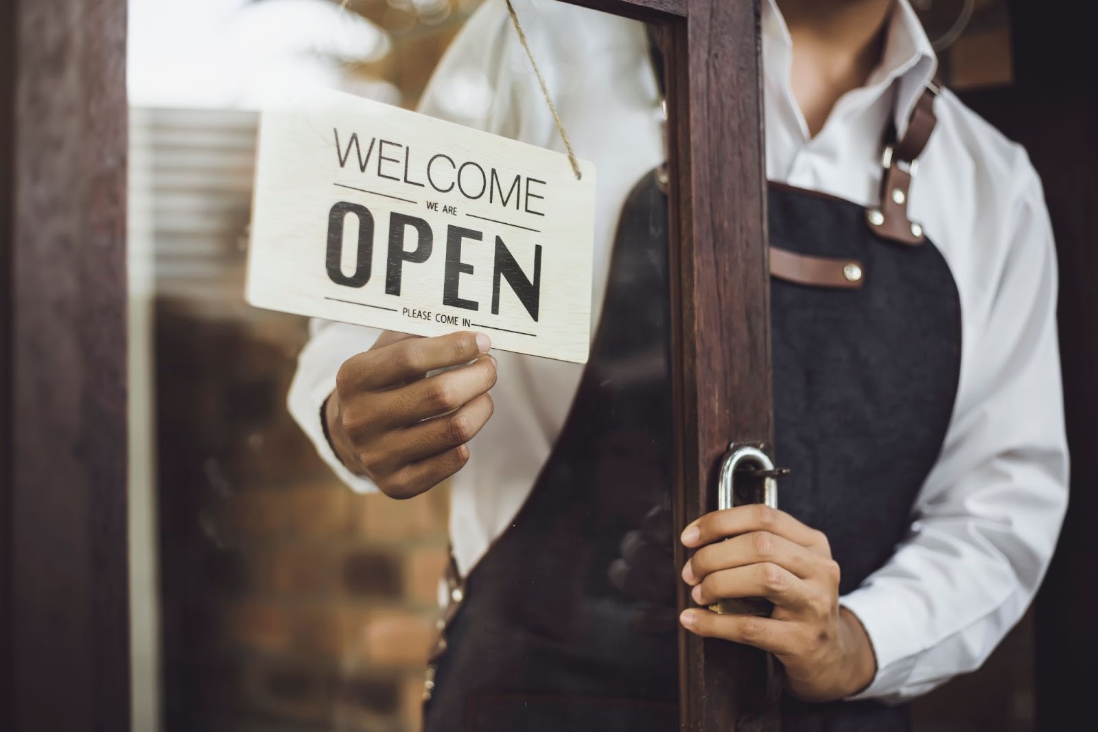 A cropped photo of a restaurant owner hanging the “open” sign