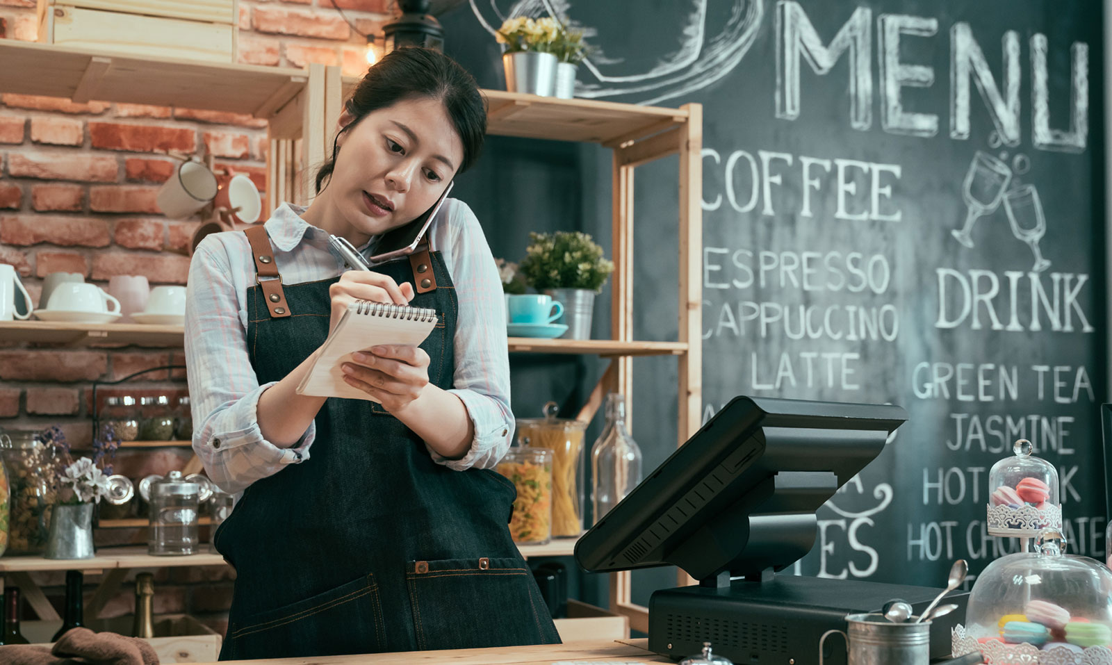 An owner of a restaurant taking notes while on the phone