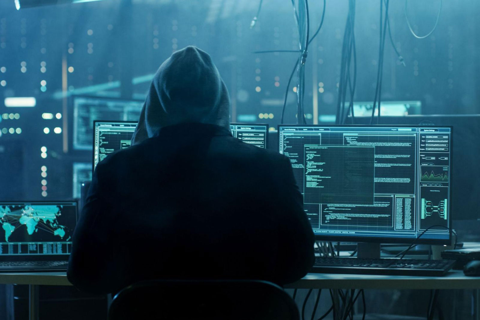 A photo of a hooded hacker at their computer desk