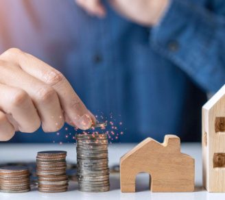 A stack of coins next to a miniature house and building, representing tax on rental income Ontario