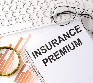 A flatlay shot showing a keyboard, glasses, charts, and the word “Insurance Premium” on a notebook
