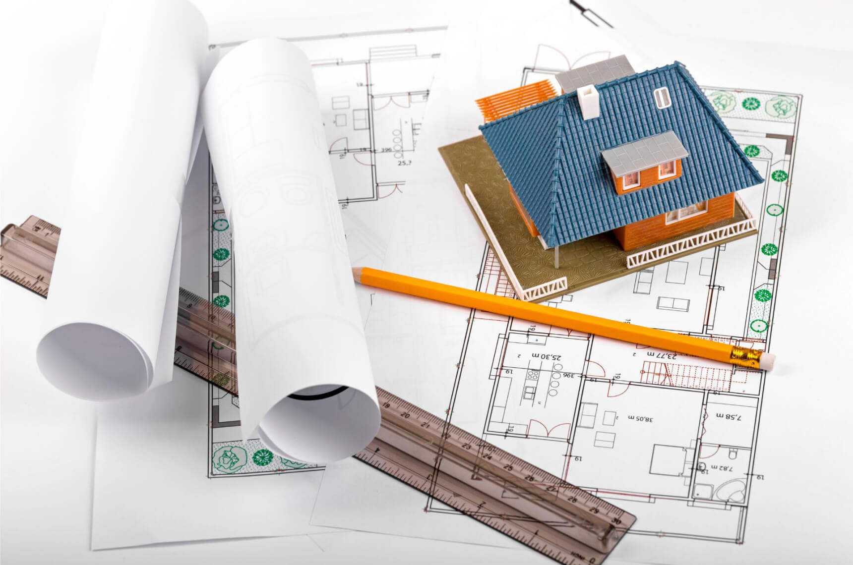 A ruler, pencil, rolled papers, and a model house on top of a blueprint