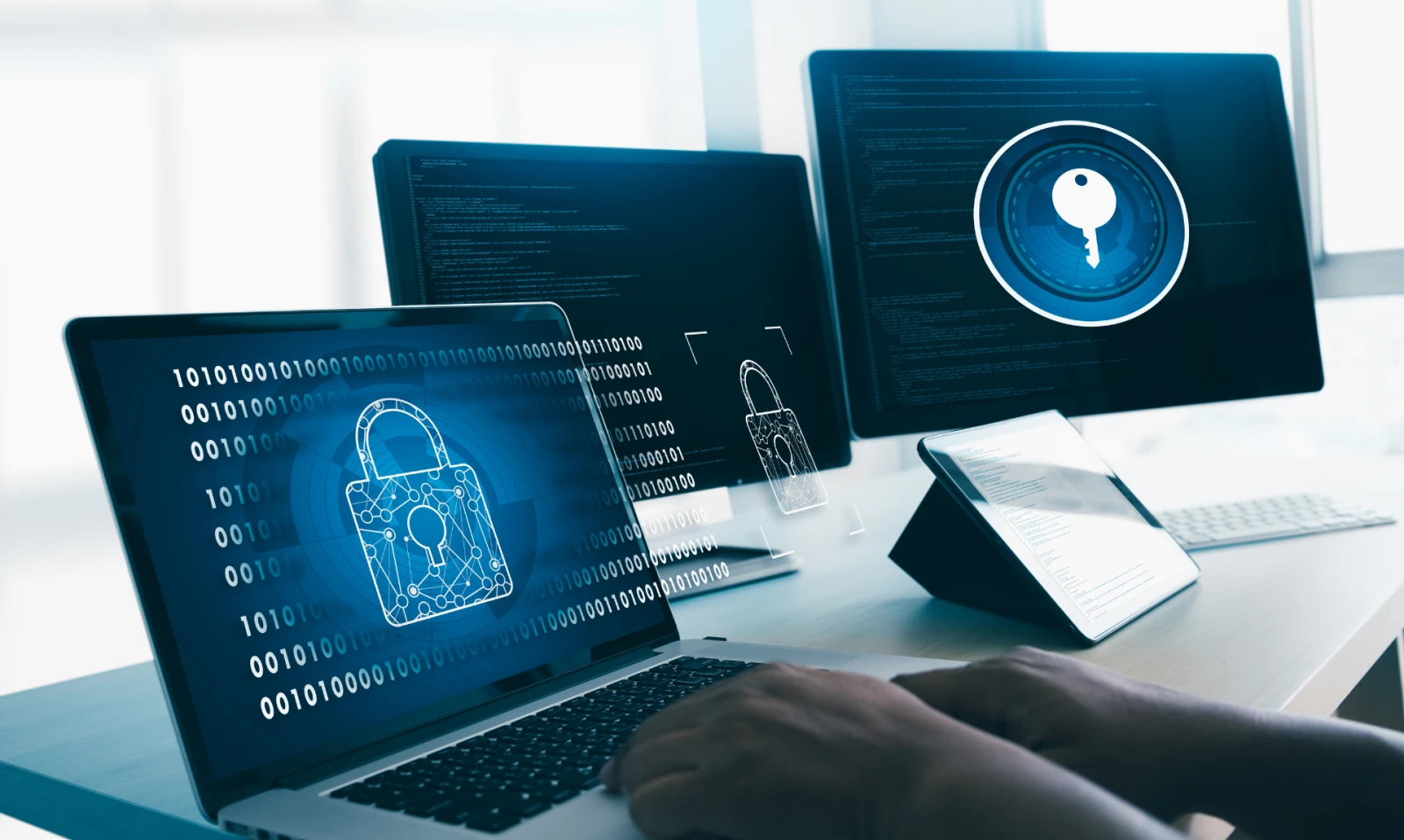 An office desk set-up with two monitors, a laptop, and a tablet showing cybersecurity measures in place