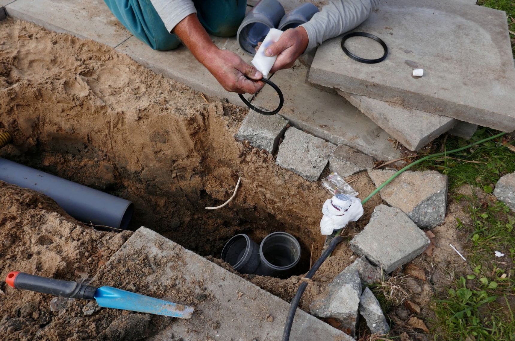 A contractor surrounded by tools laying and installing a sewer pipe in the ground