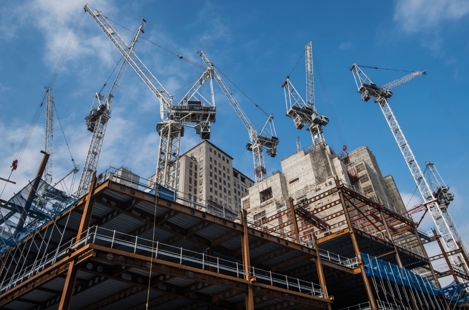 Several cranes surrounding a multi-story building under construction