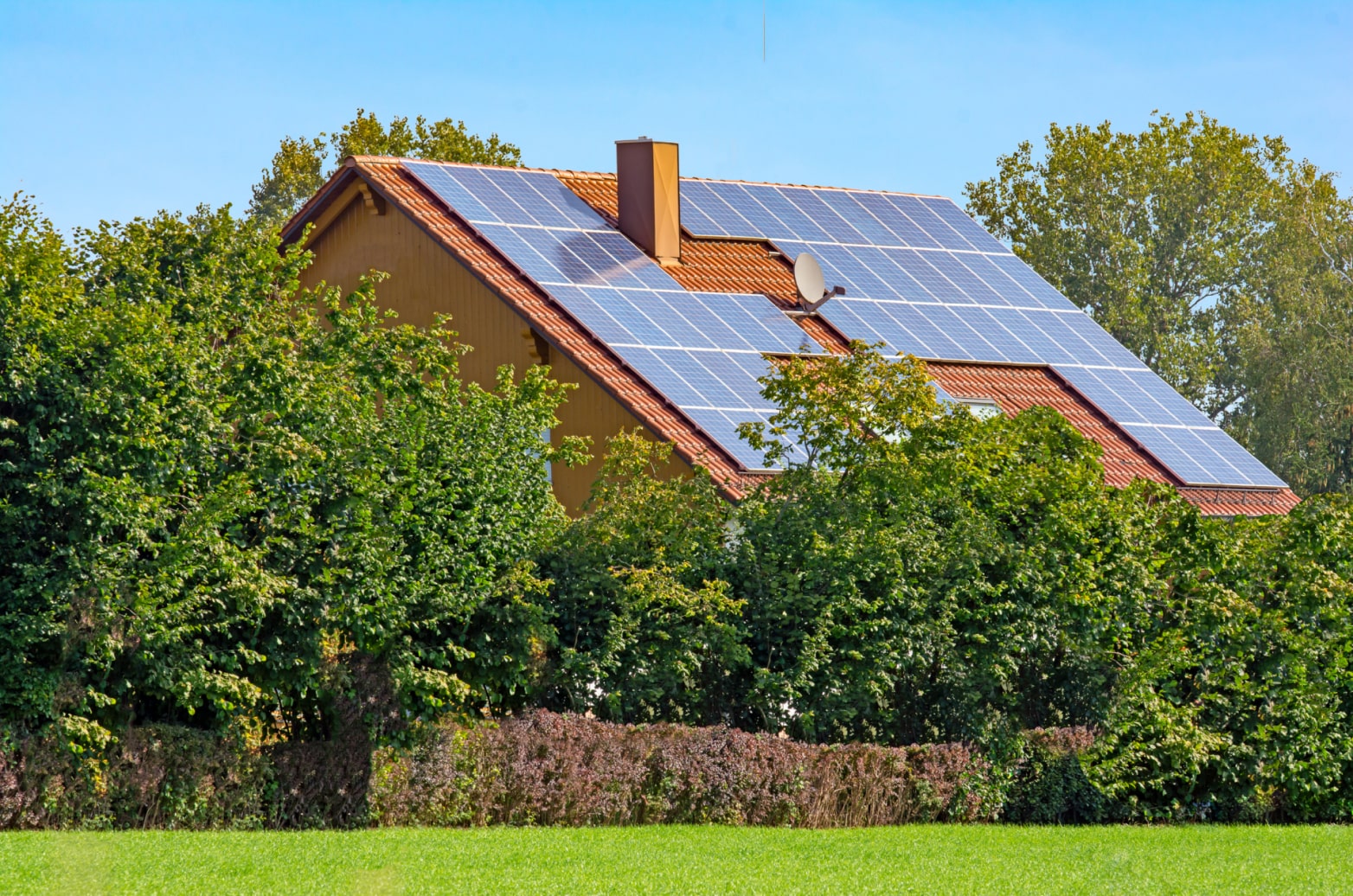 A home surrounded by shrubbery with solar panels on the roof
