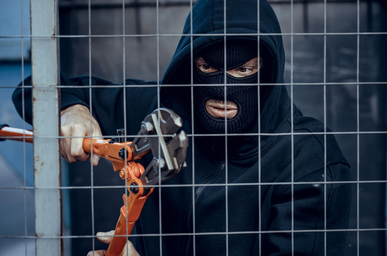 Thief breaking into a construction site with wire cutters about to cut through a fence