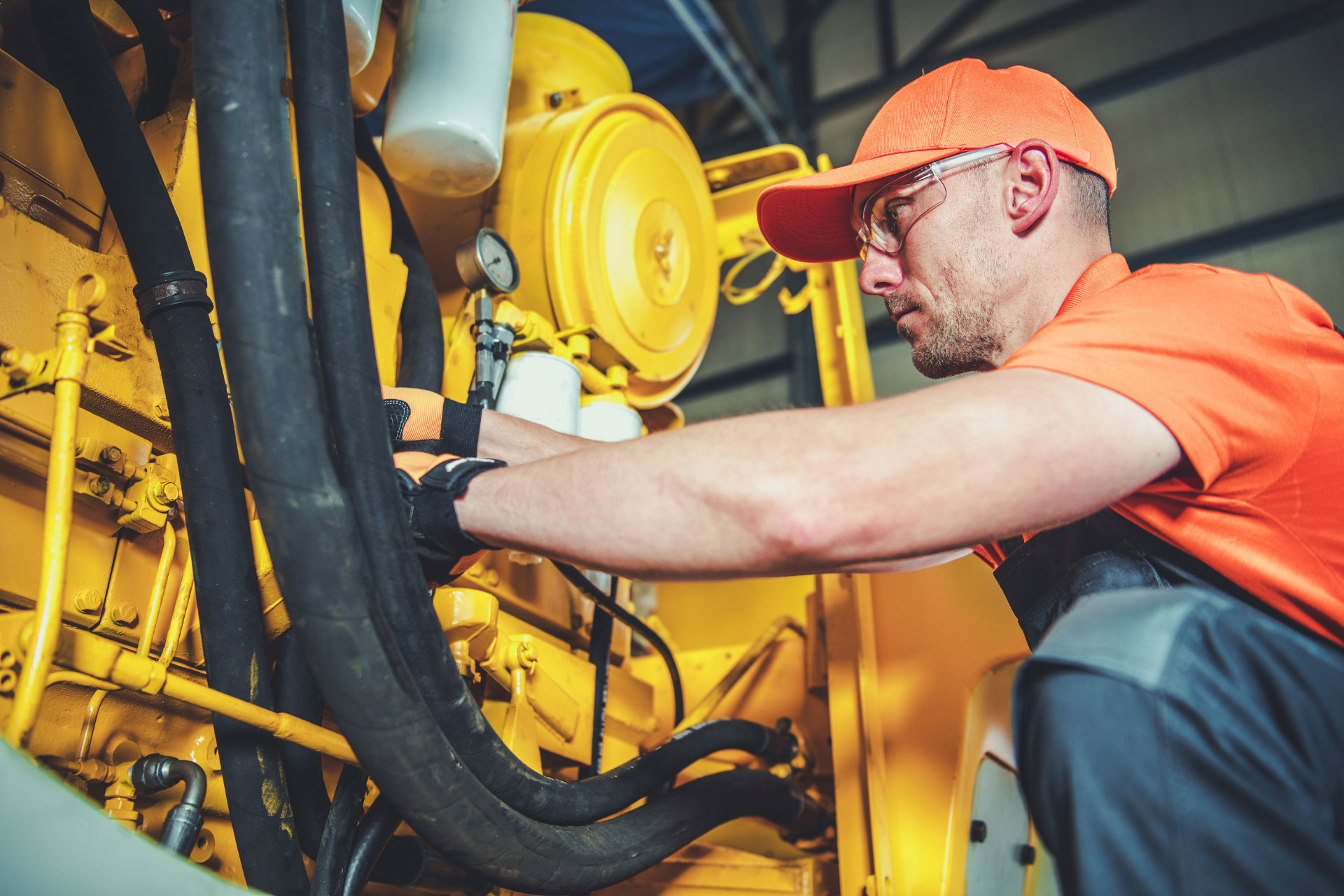 Mechanic wearing and orange shirt and safety goggles performing preventive maintenance on heavy equipment