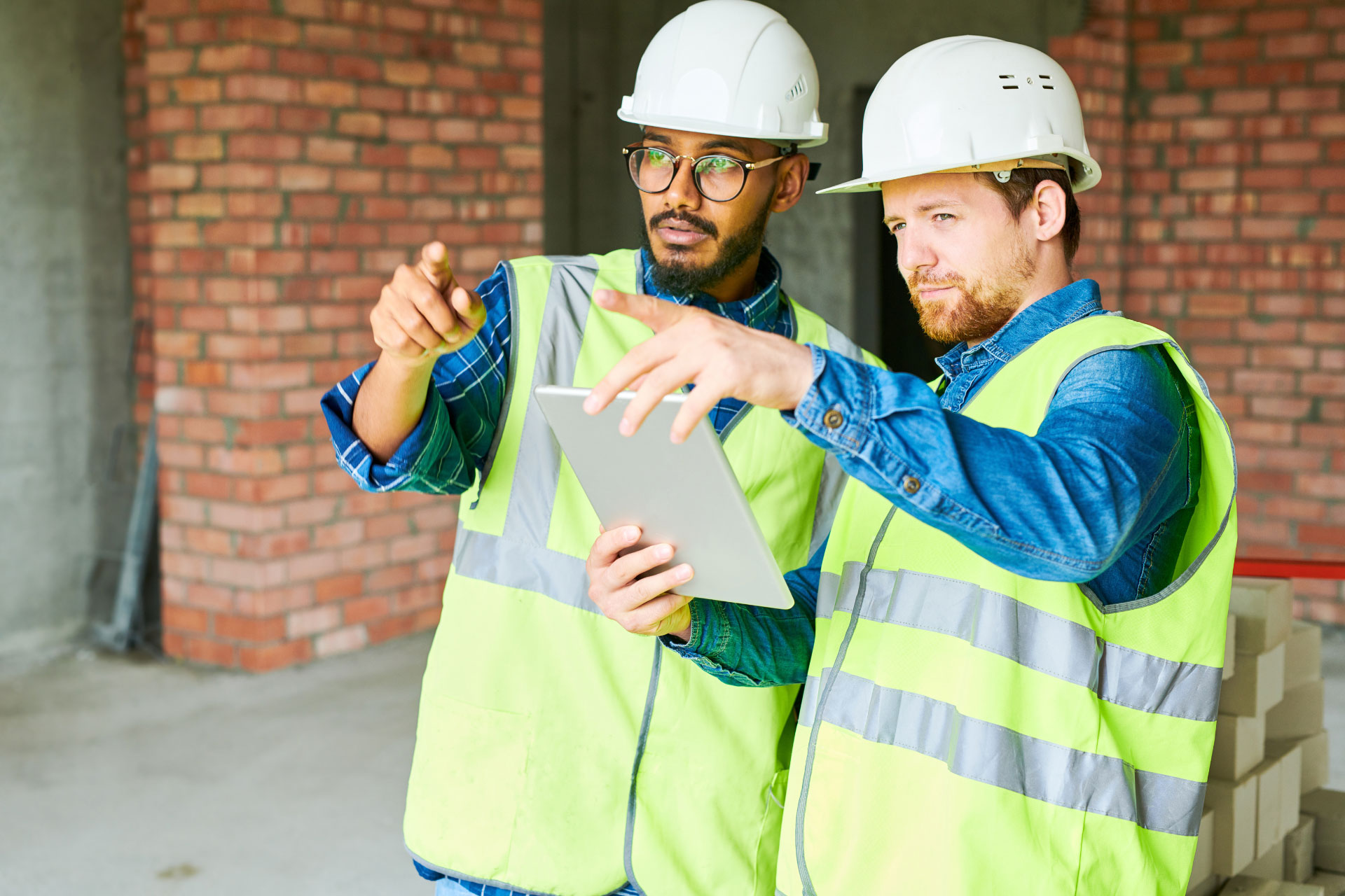 Construction project managers wearing safety gear use an AI app on a tablet
