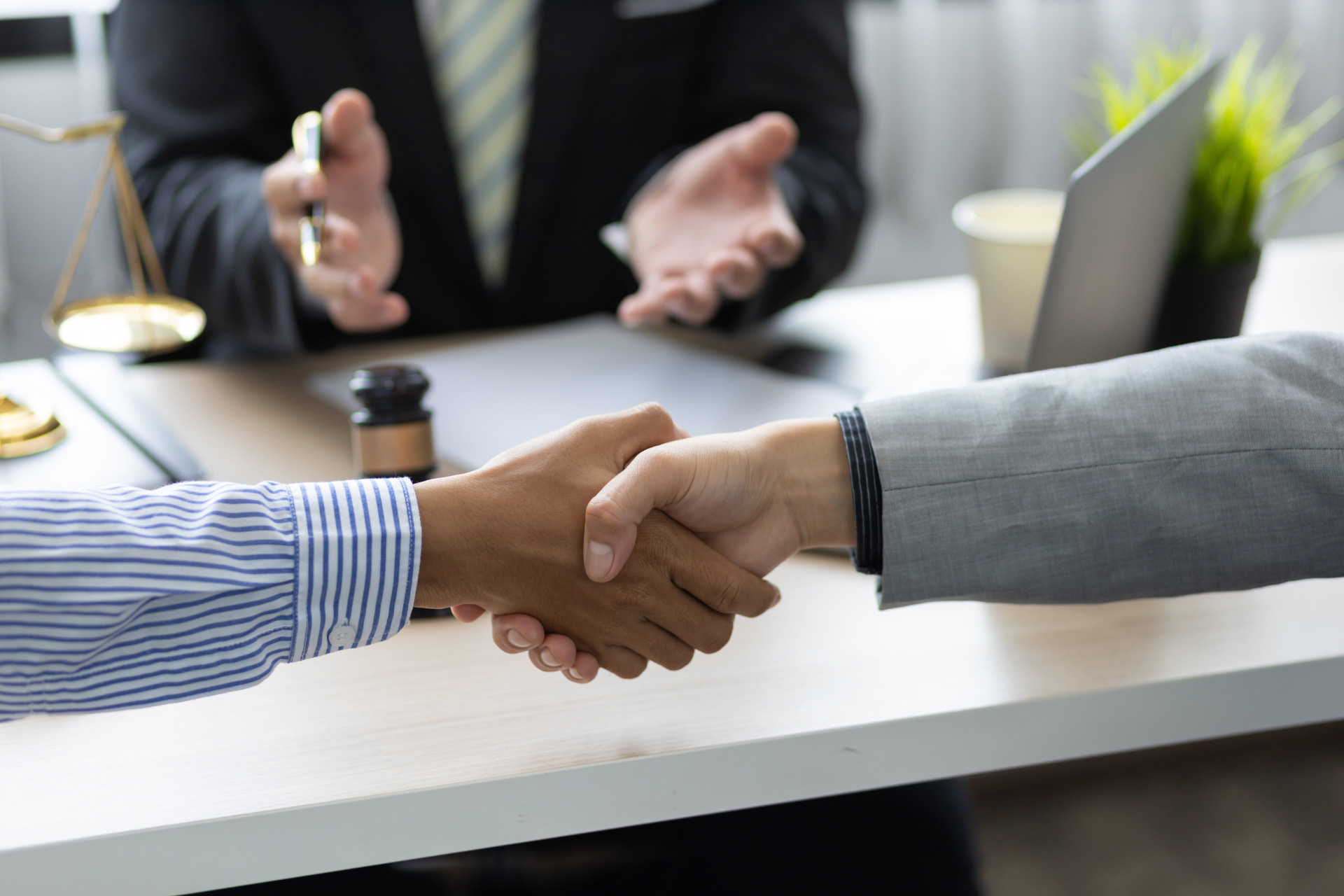 Two people shake hands to settle a legal dispute with a lawyer mediating in the background
