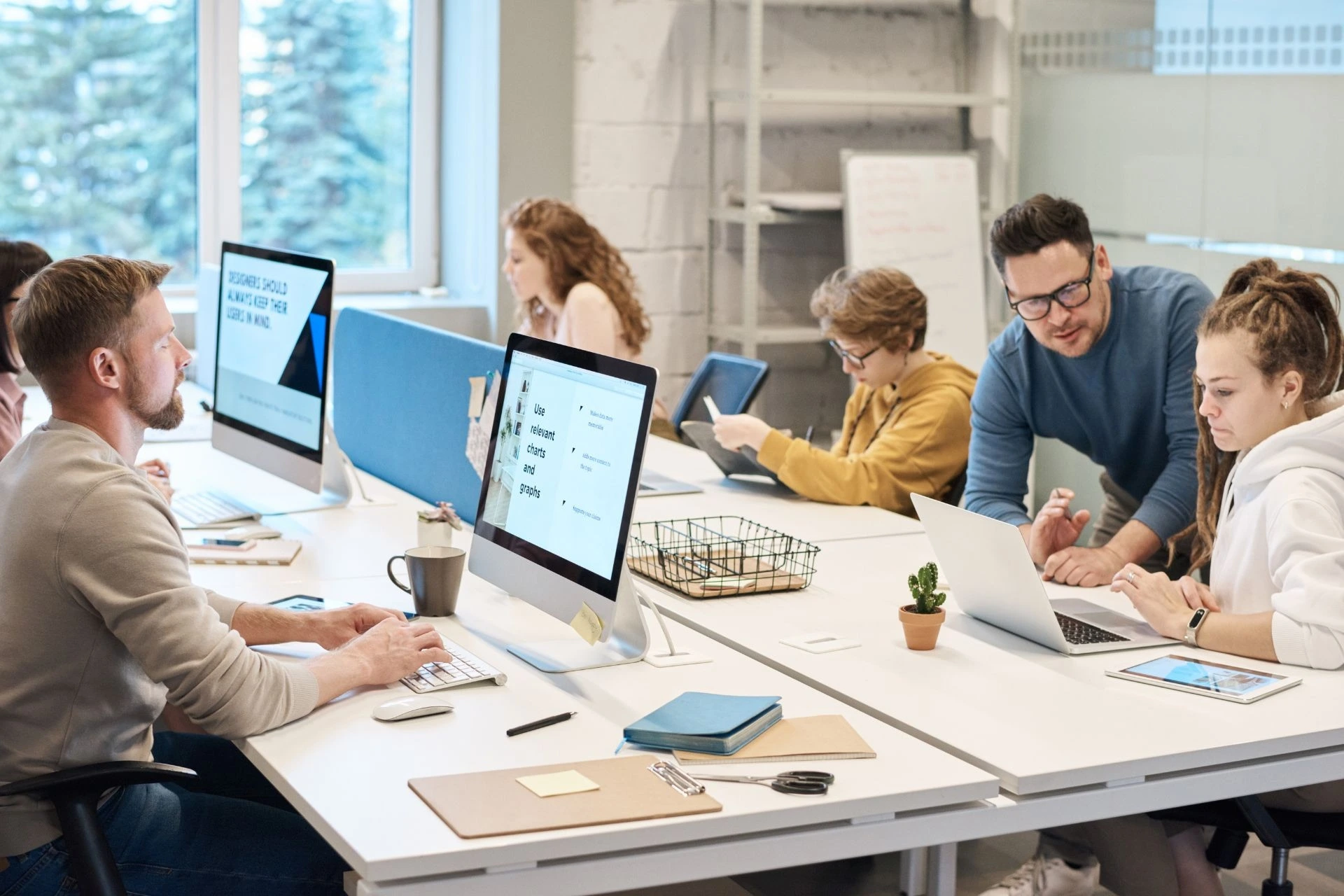 An open office with employees seated on two long tables working on their computers