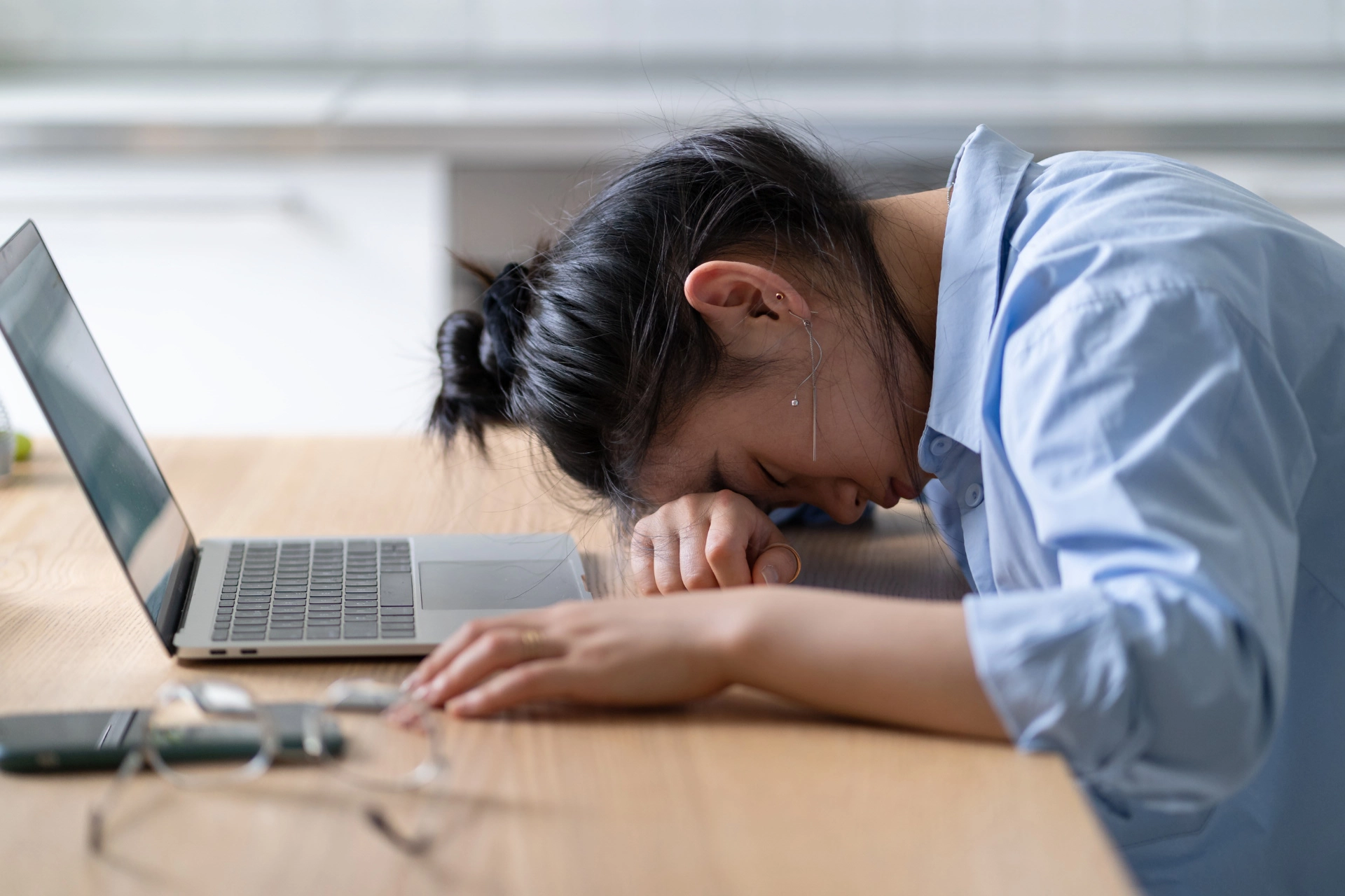  A woman experiencing burnout or stress rests her head on her desk in front of her laptop.