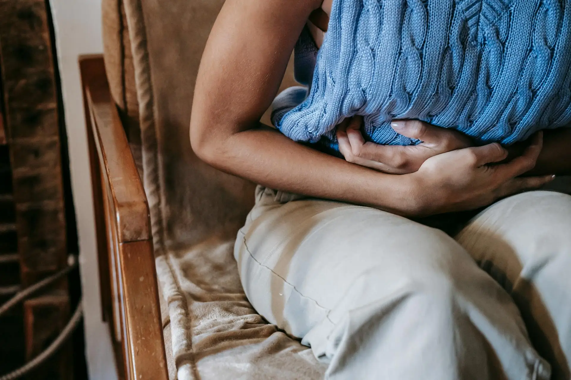 Woman in blue sweater holding her stomach in pain