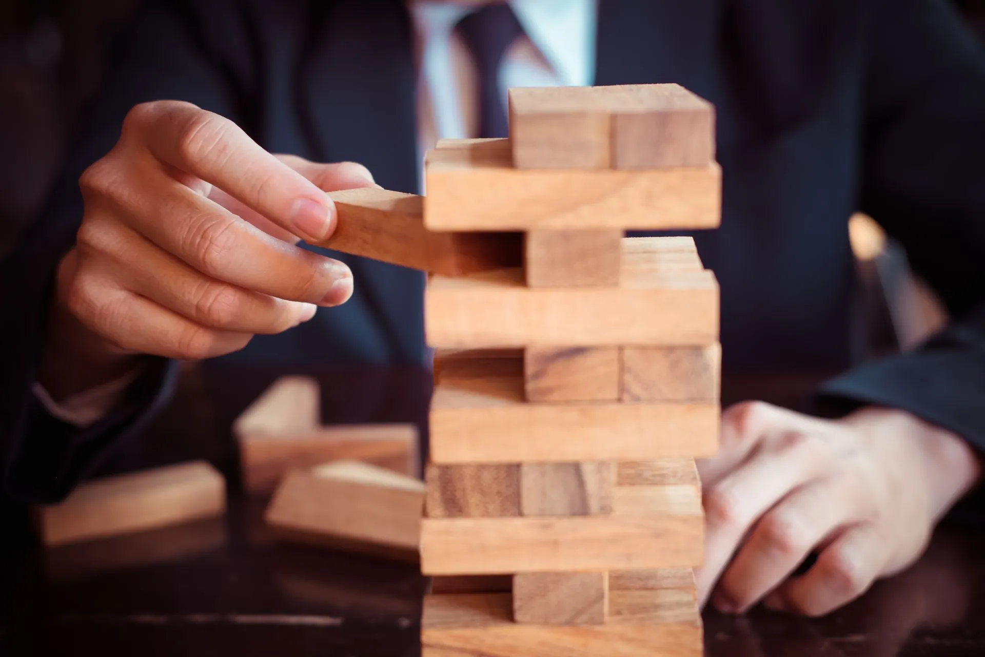 A businessman placing a wooden block on a tower, signifying risk management