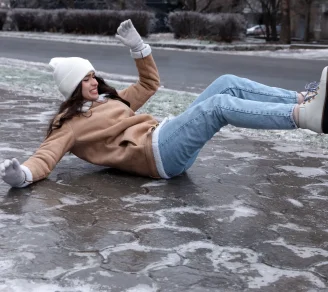 A woman in winter gear is slipping on an icy sidewalk
