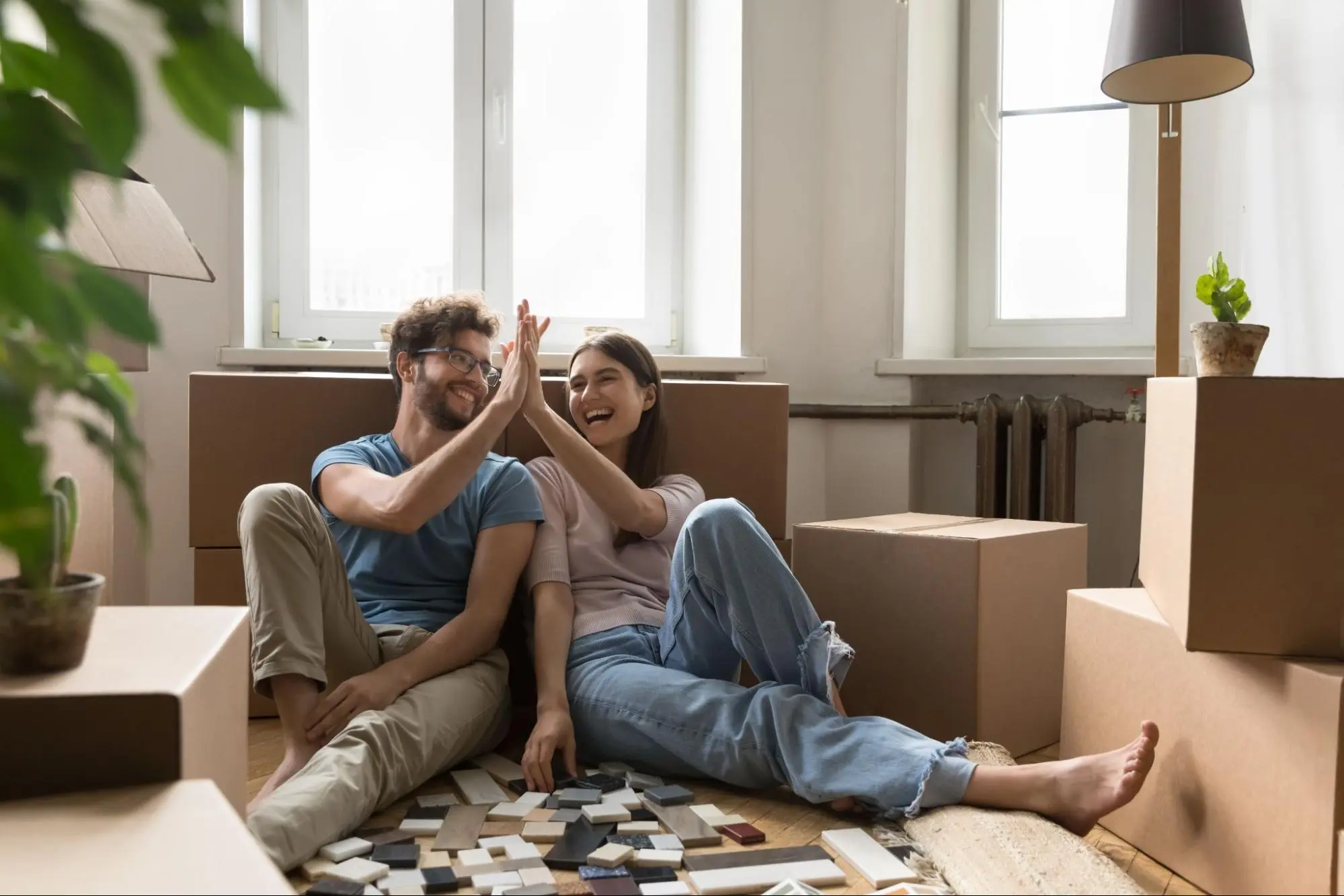 A young couple surrounded by boxes, smiles and high-fives in their new apartment.
